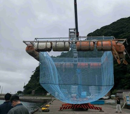 クレーンで釣り上げられる生簀の画像